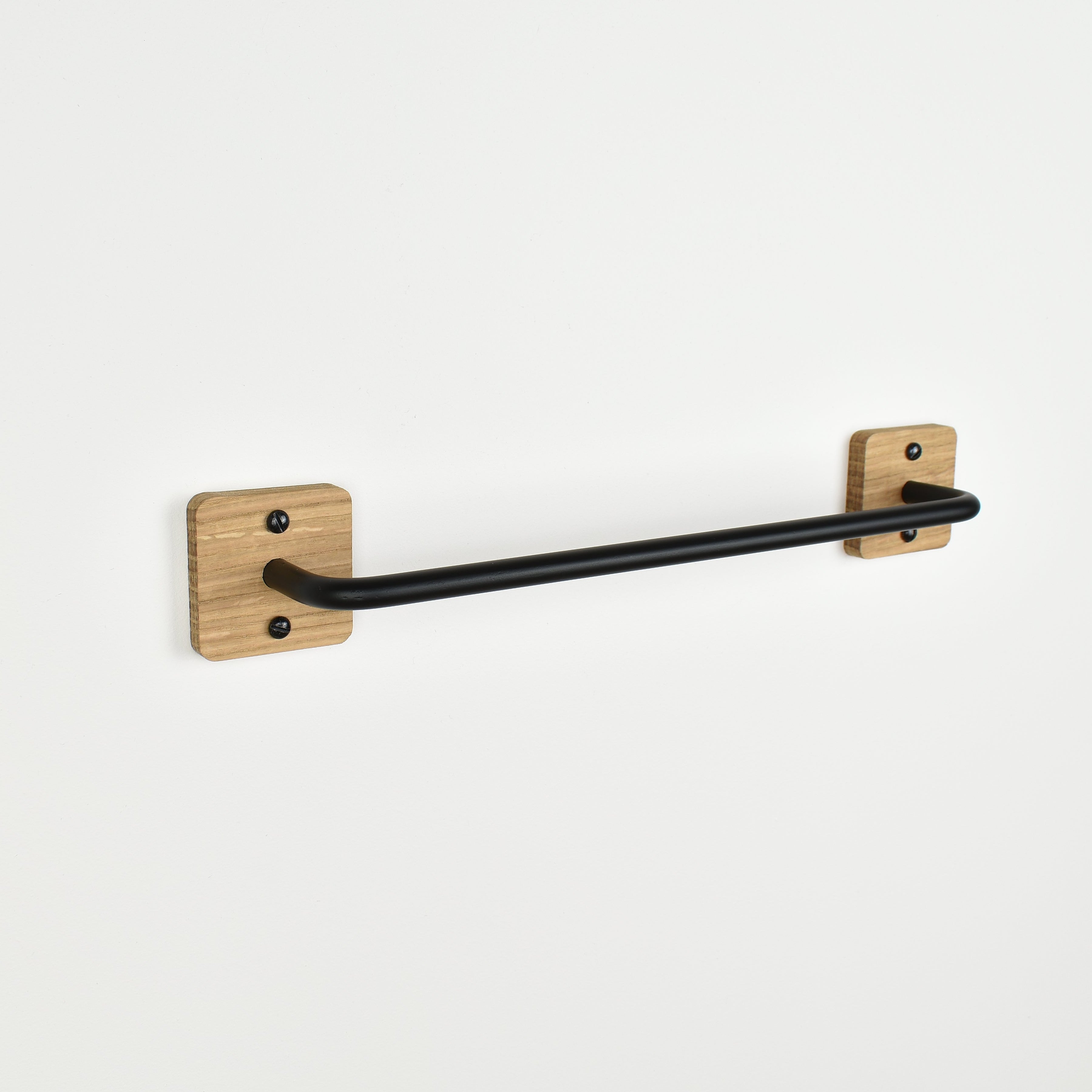 Black towel bar mounted on a white wall with oak fixings.