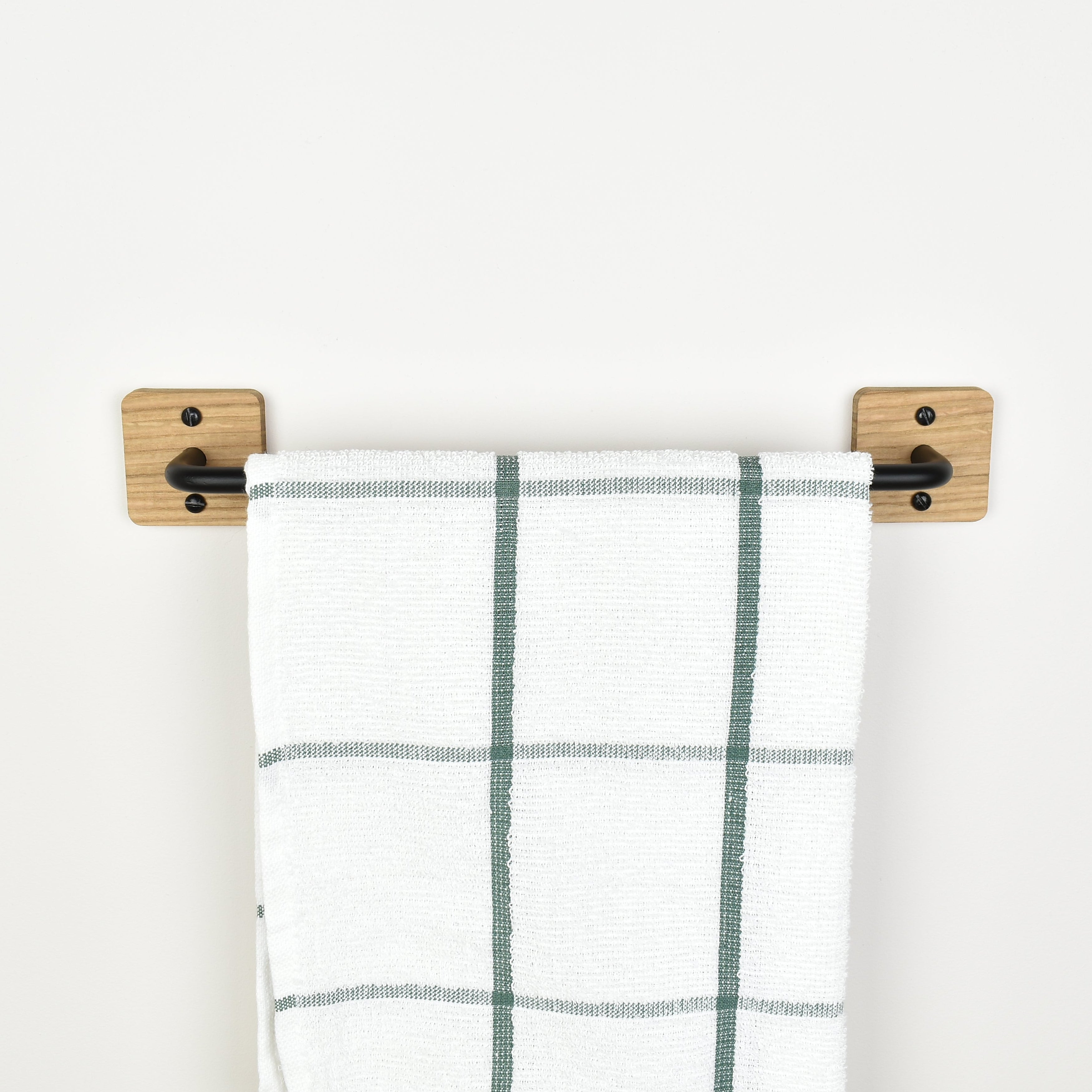 Plaid towel hanging on a oak and black metal rail against a white background
