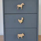 Oak farm animal drawer knobs fitted to a blue chest of drawers showing horse, chicken and cow designs