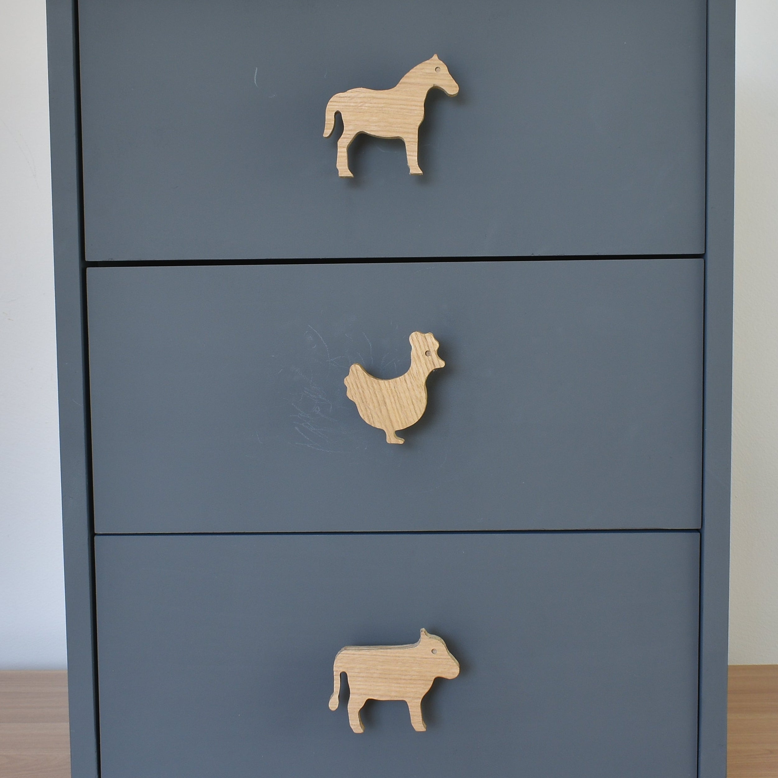 Oak farm animal drawer knobs fitted to a blue chest of drawers showing horse, chicken and cow designs