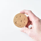 Hand holding handmade oak moon drawer knob showing crater detail and natural wood grain