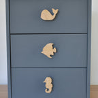 Oak ocean animal drawer knobs fitted to a blue chest of drawers showing whale, fish and seahorse designs