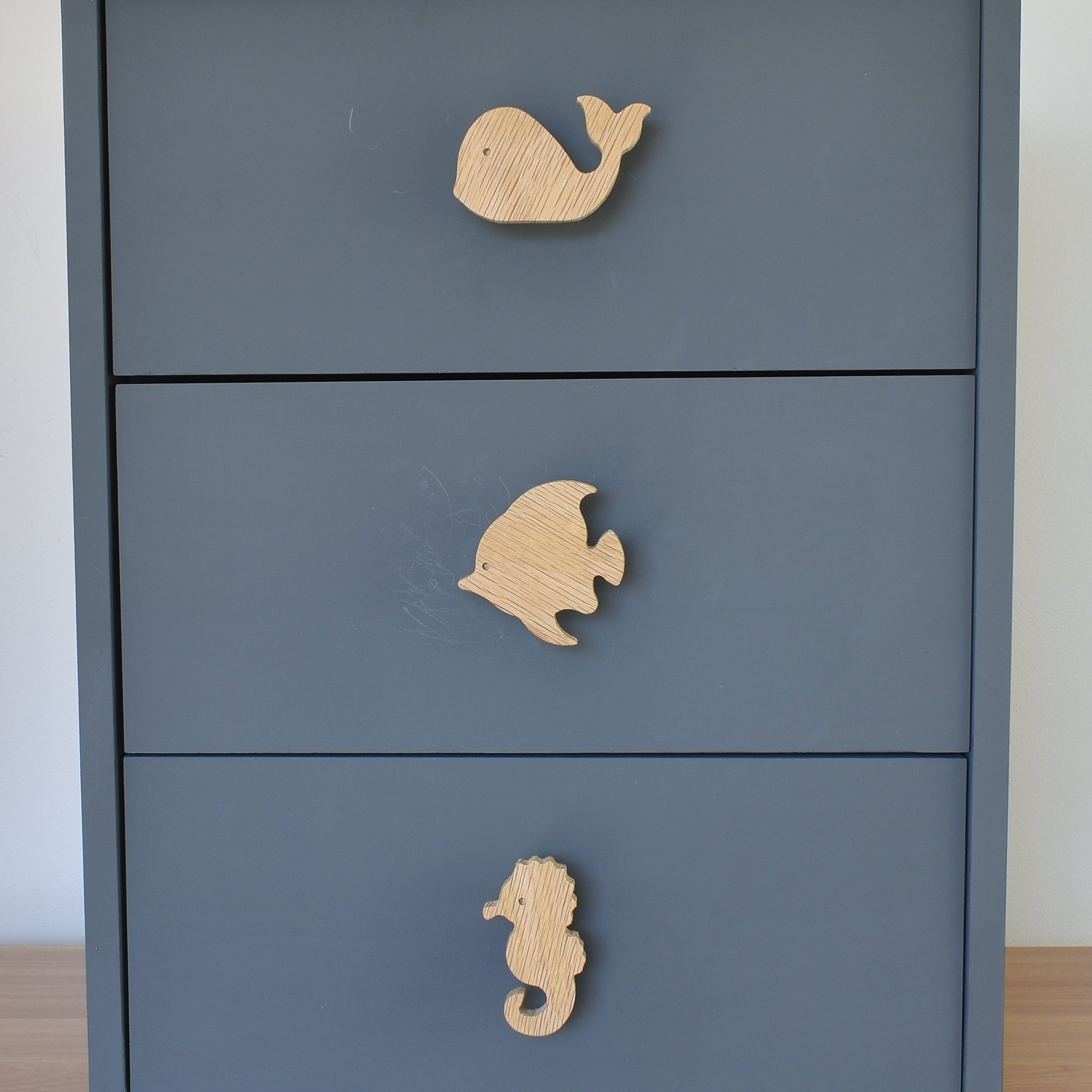 Oak ocean animal drawer knobs fitted to a blue chest of drawers showing whale, fish and seahorse designs