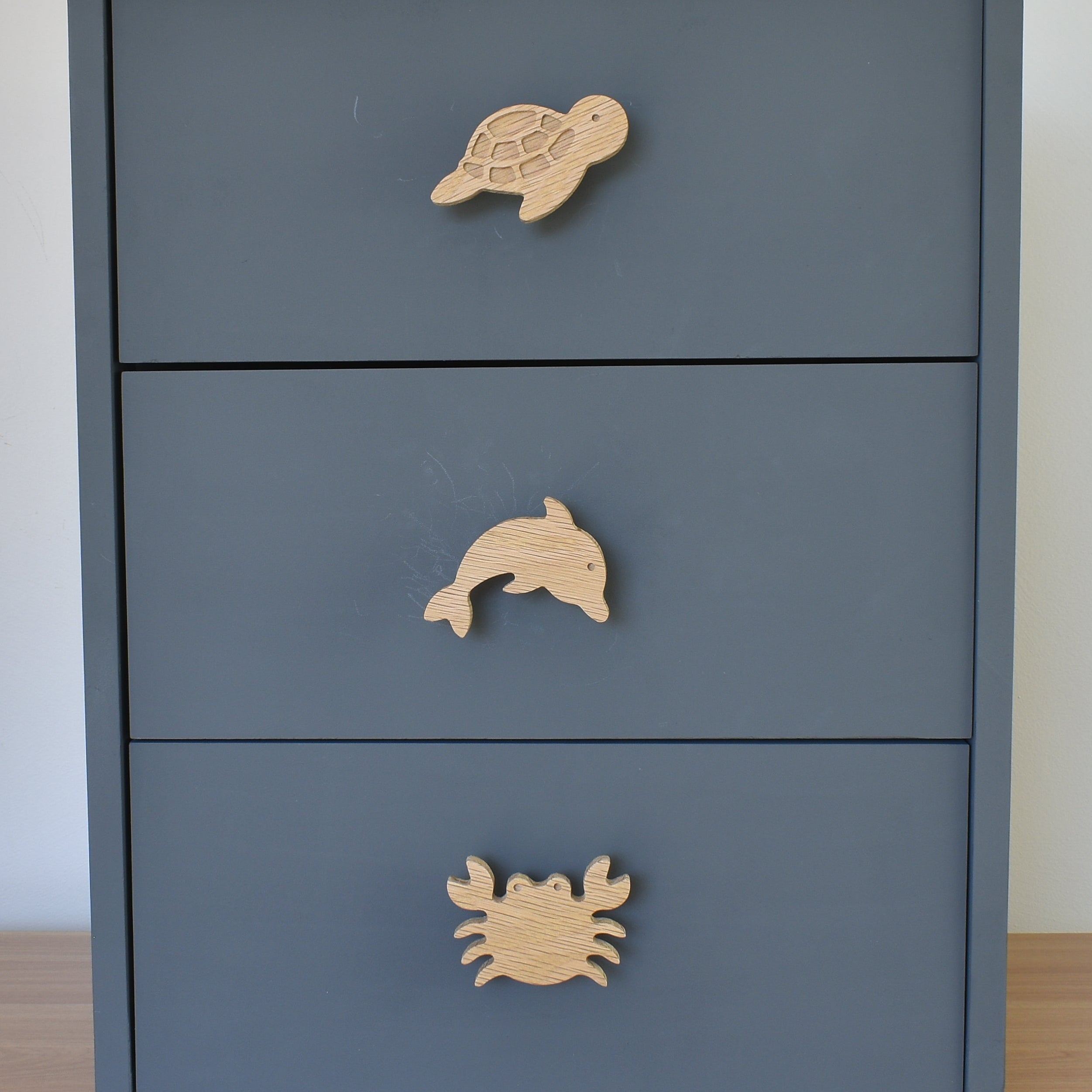 Oak ocean animal drawer knobs fitted to a blue chest of drawers showing turtle, dolphin and crab designs