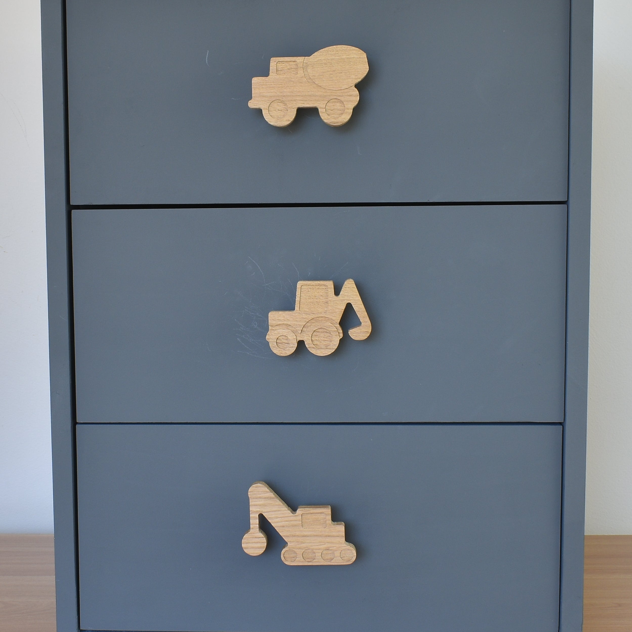 Oak construction vehicle drawer knobs fitted to a blue chest of drawers showing cement truck, digger and crane designs