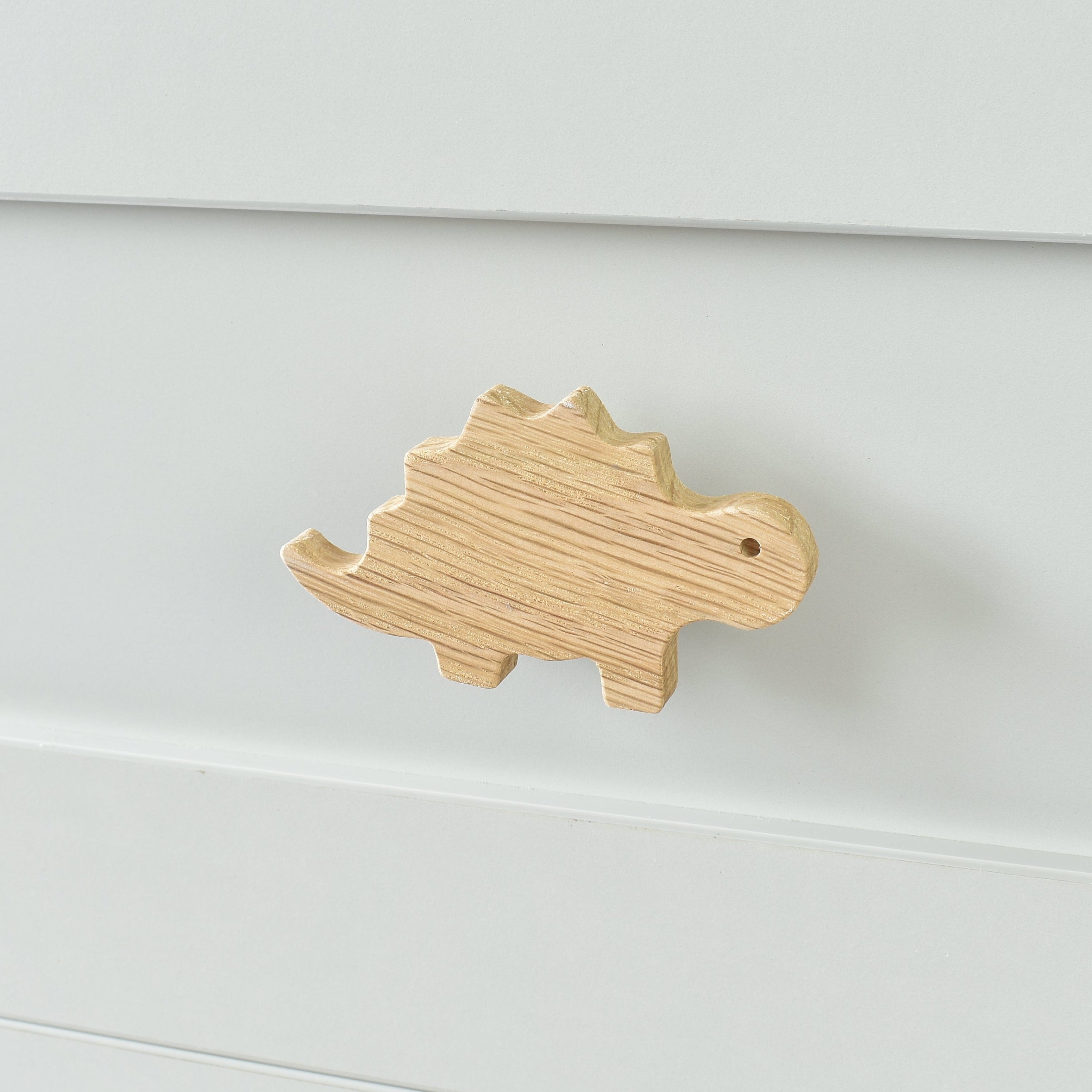 Oak stegosaurus drawer knob fitted to a white chest of drawers showing natural wood grain