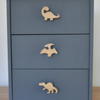 Oak dinosaur drawer knobs fitted to a blue chest of drawers showing brachiosaurus, pterodactyl and spinosaurus designs