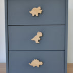 Oak dinosaur drawer knobs fitted to a blue chest of drawers showing triceratops, T rex and stegosaurus designs