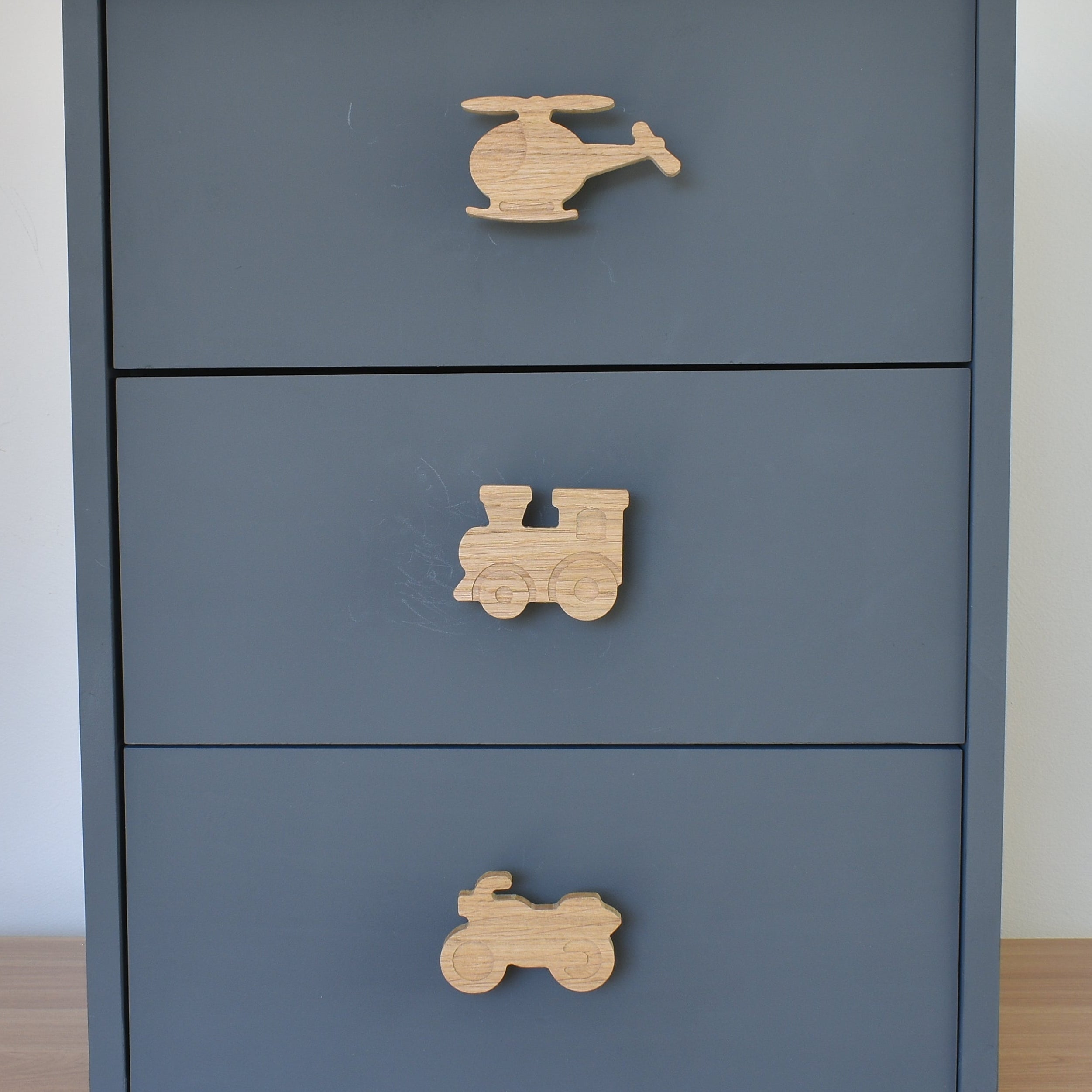 Oak transport vehicle drawer knobs fitted to a blue chest of drawers showing helicopter, train and motorbike designs