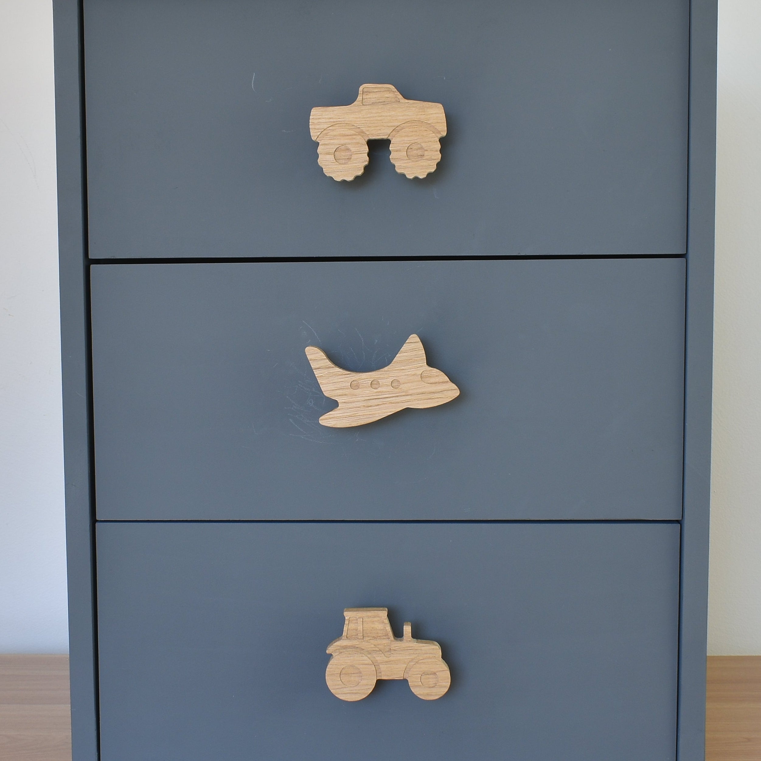 Oak transport vehicle drawer knobs fitted to a blue chest of drawers showing monster truck, aeroplane and tractor designs
