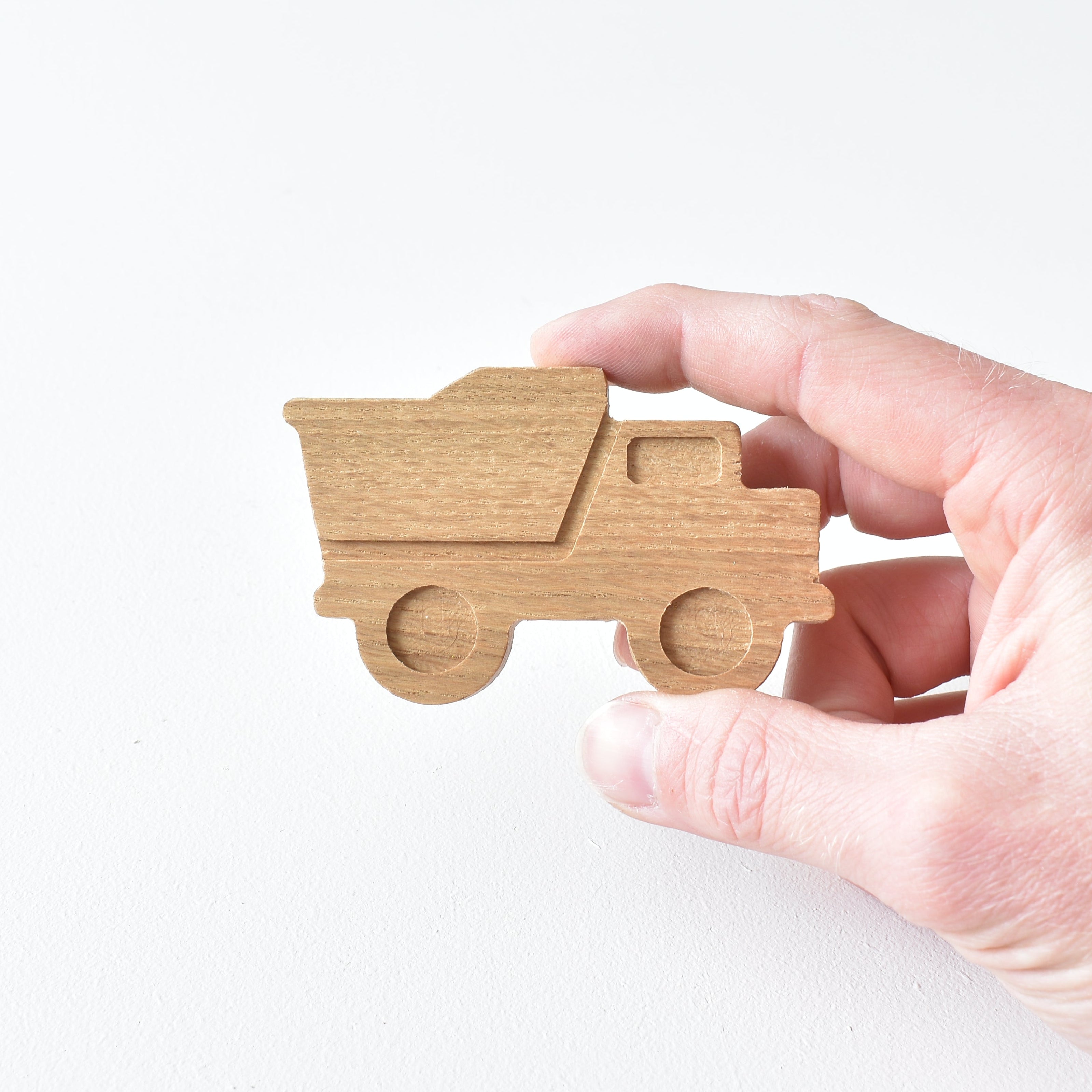 Hand holding handmade oak dump truck drawer knob showing raised detail and natural wood grain