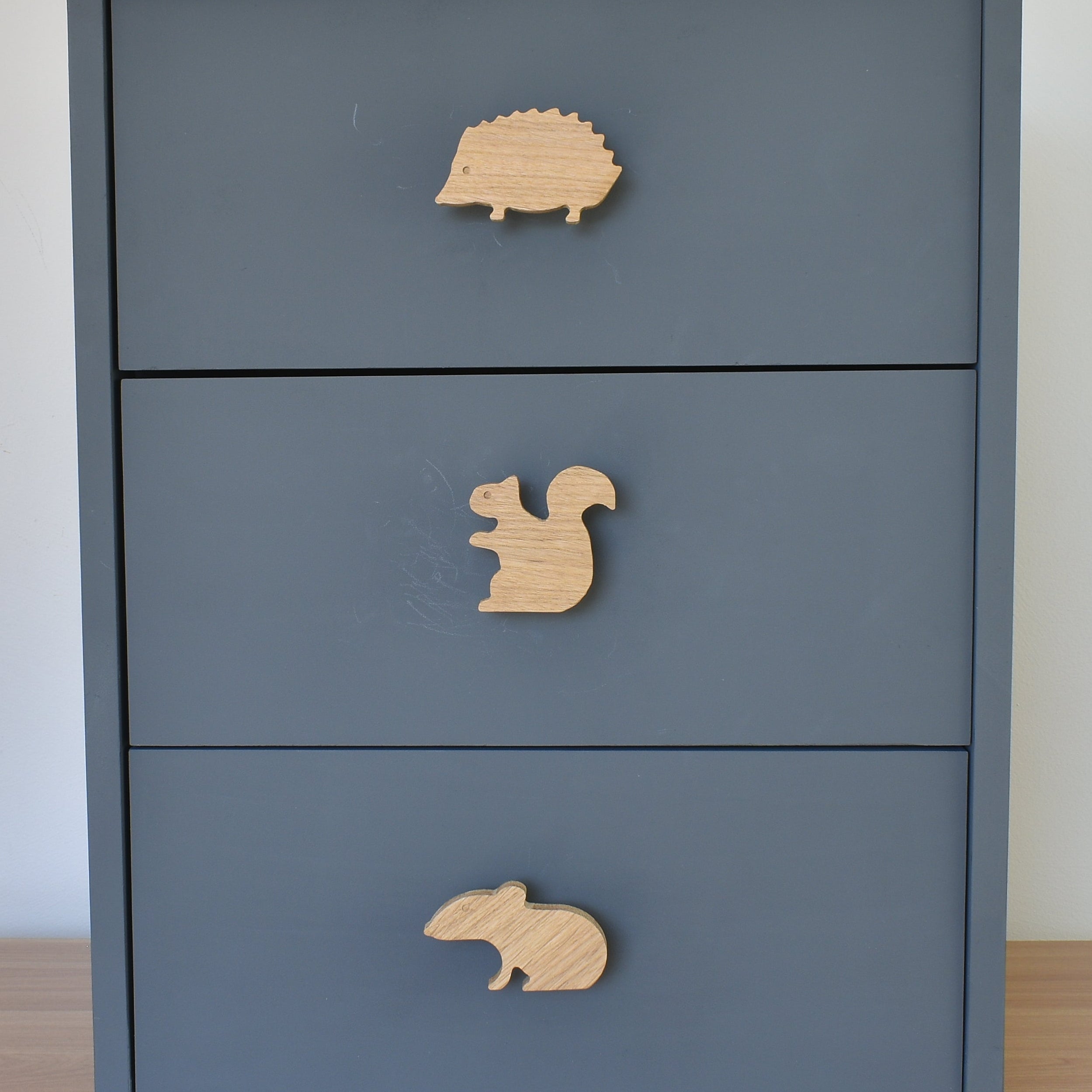 Oak woodland animal drawer knobs fitted to a blue chest of drawers showing hedgehog, squirrel and mouse designs
