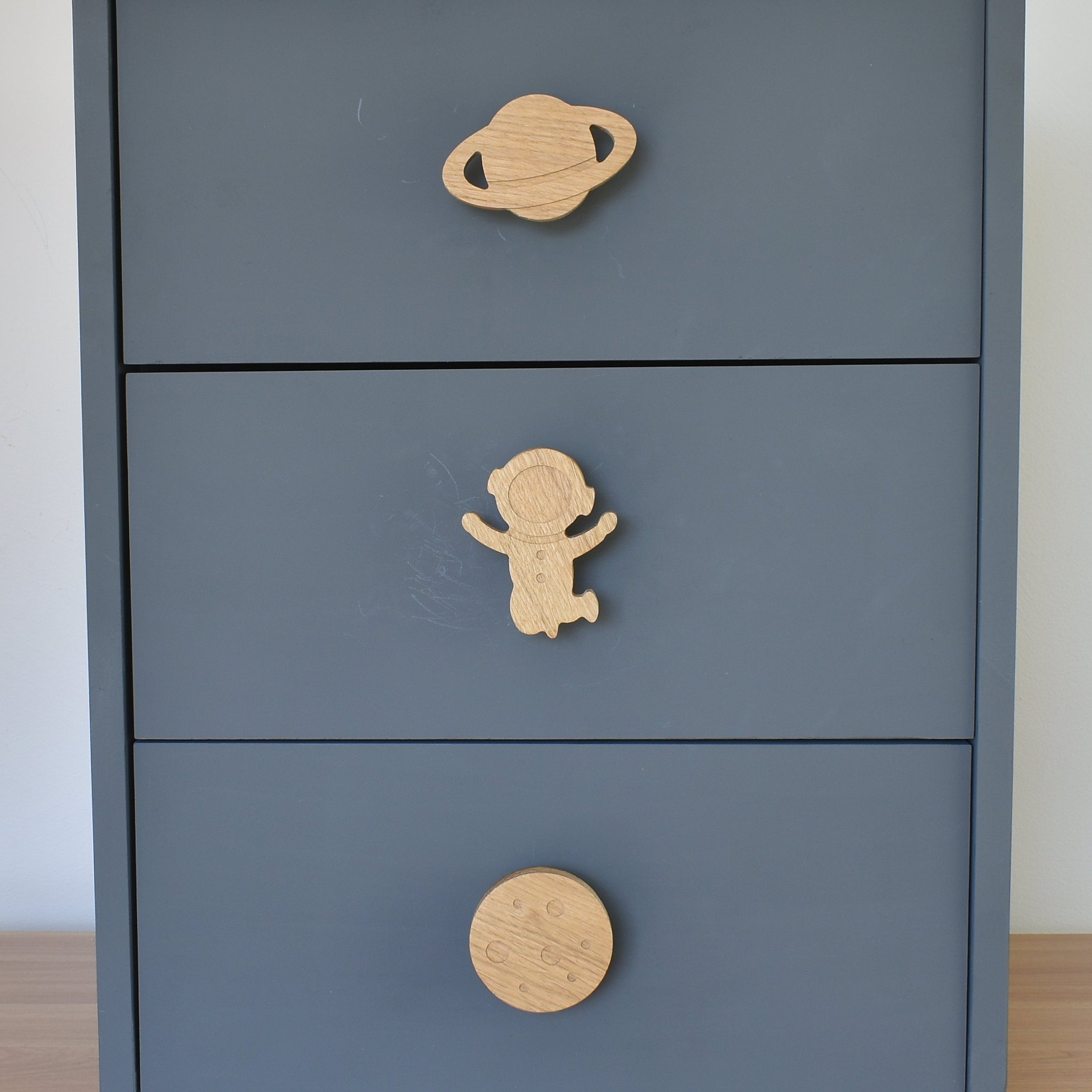 Oak space themed drawer knobs fitted to a blue chest of drawers showing planet, astronaut and moon designs