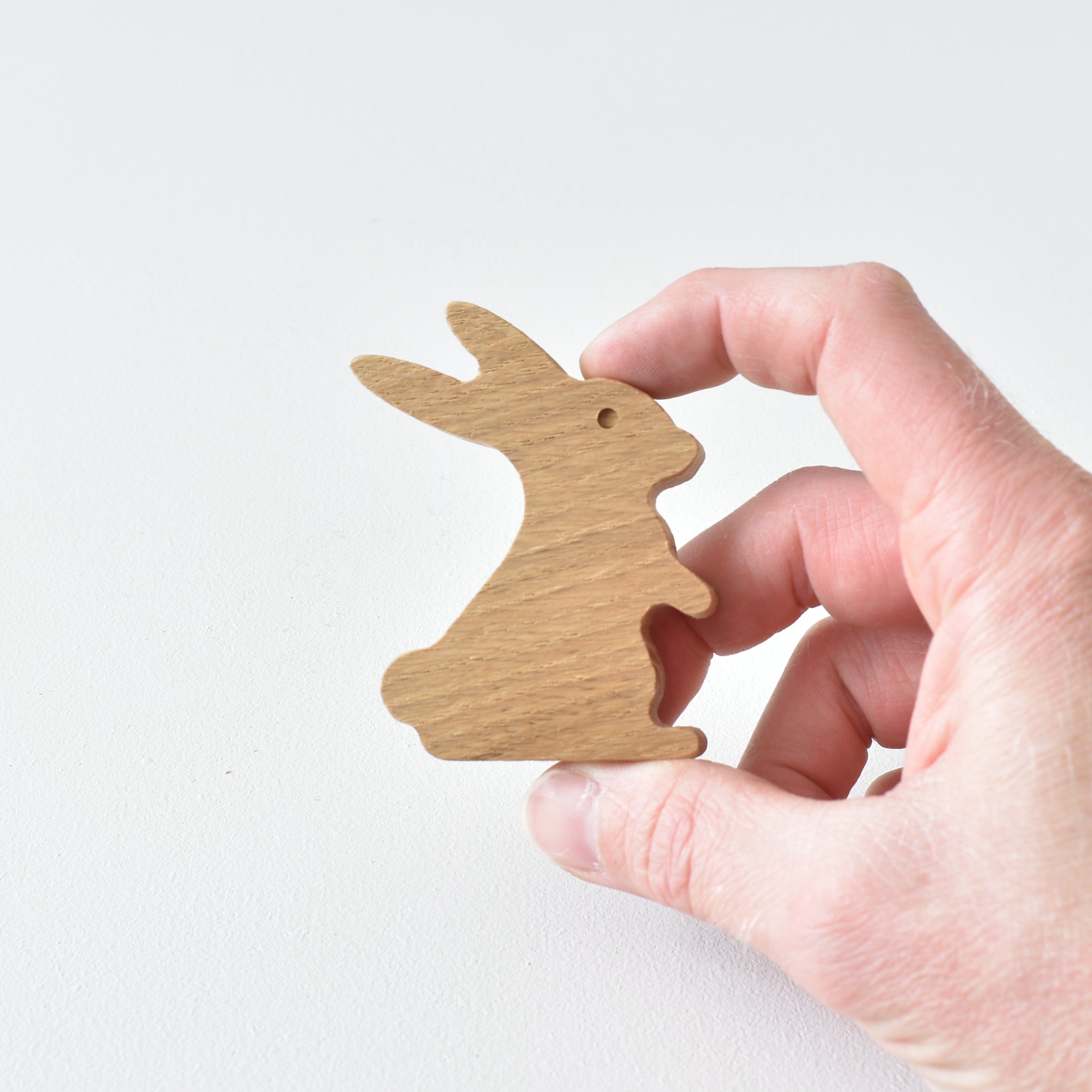 Hand holding handmade oak rabbit drawer knob showing natural wood grain and woodland animal shape