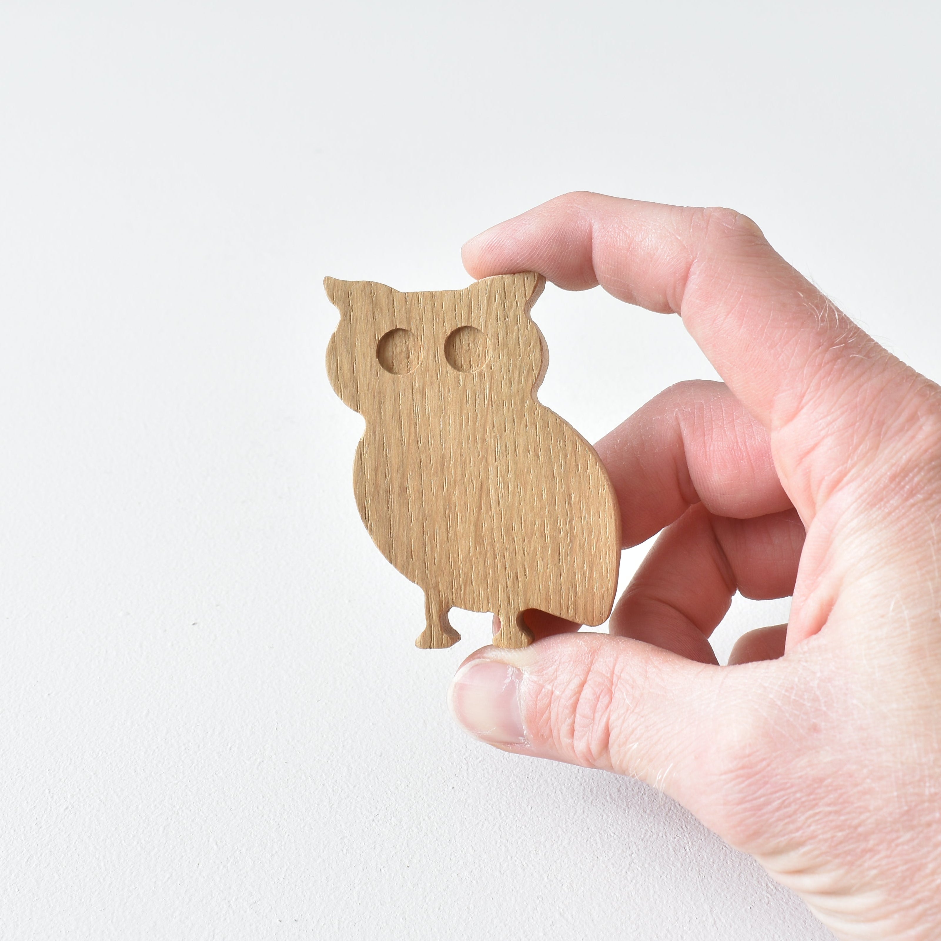 Hand holding handmade oak owl drawer knob showing natural wood grain and woodland animal shape