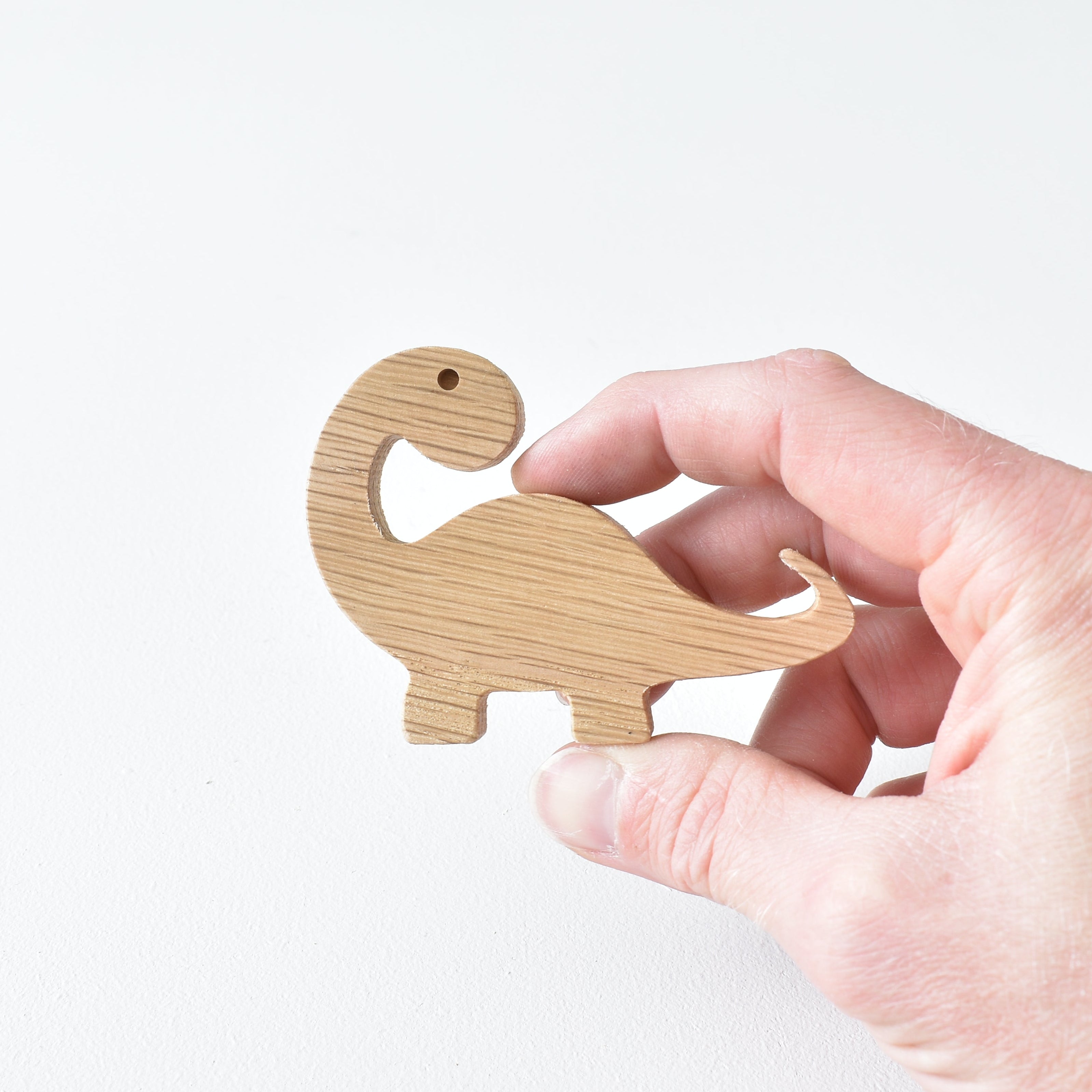 Hand holding handmade oak brachiosaurus drawer knob showing natural wood grain and curved dinosaur shape