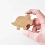 Hand holding handmade oak triceratops drawer knob showing natural wood grain and dinosaur shape