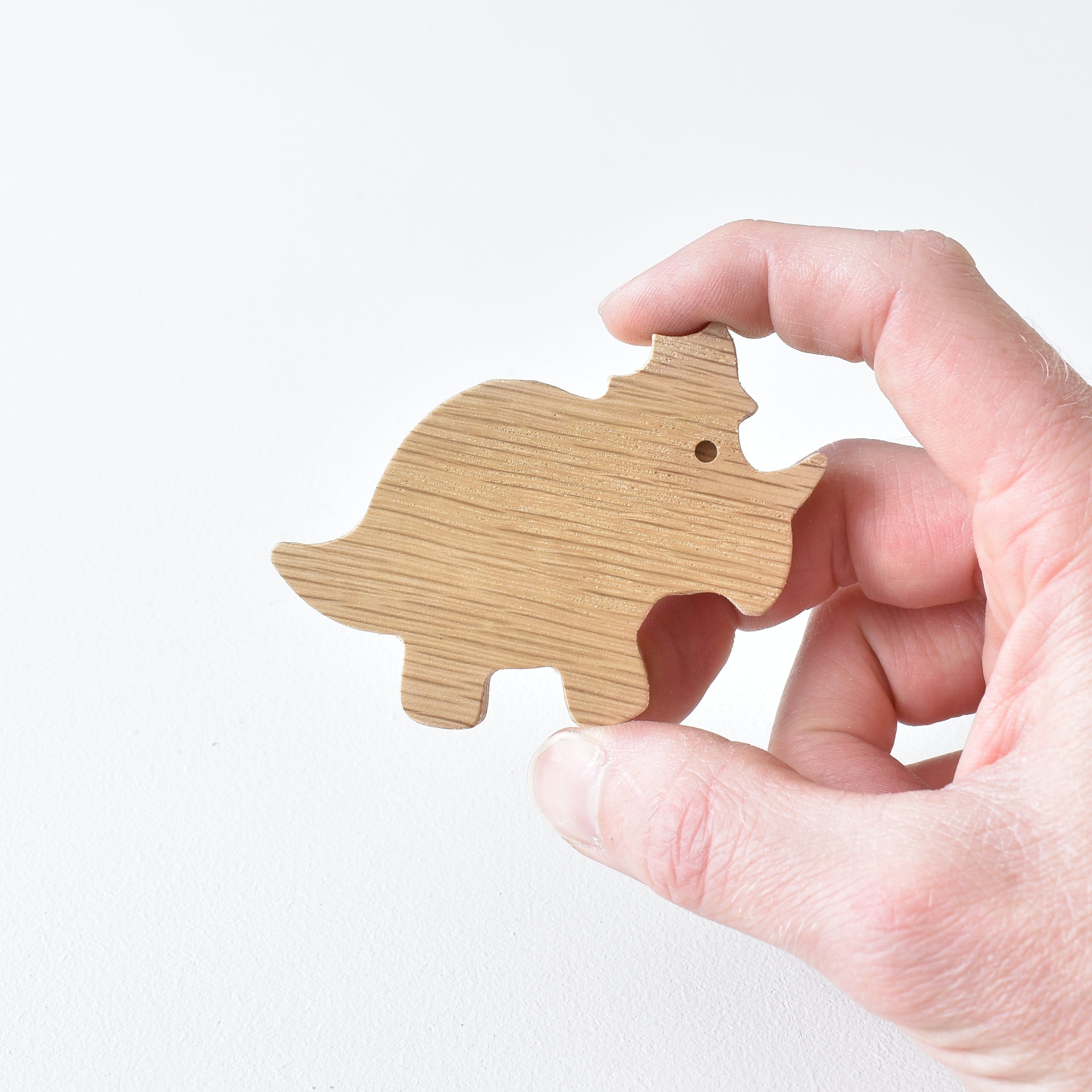 Hand holding handmade oak triceratops drawer knob showing natural wood grain and dinosaur shape