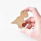 Hand holding handmade oak T rex drawer knob showing natural wood grain and dinosaur shape
