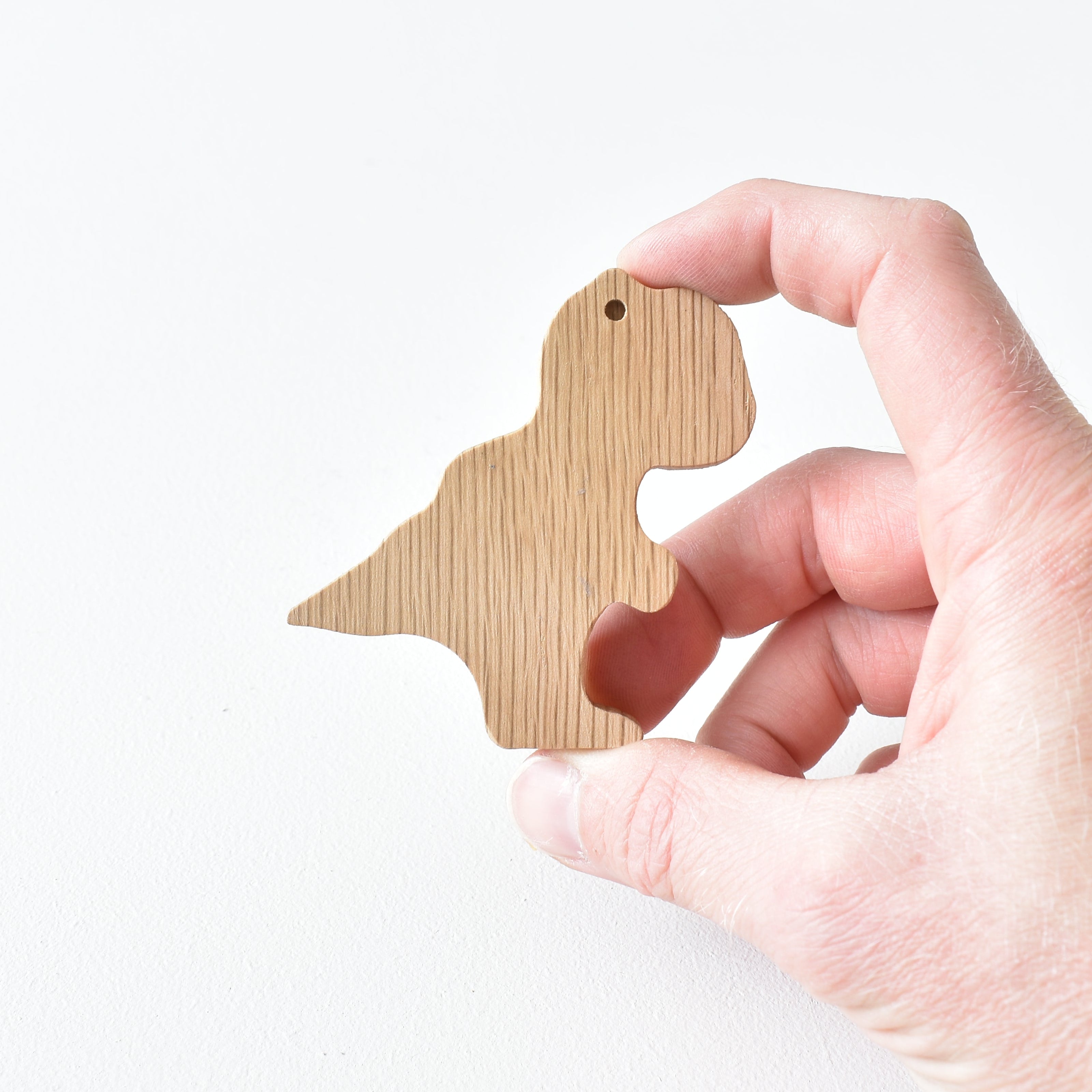 Hand holding handmade oak T rex drawer knob showing natural wood grain and dinosaur shape