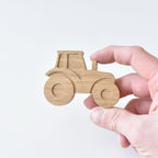Hand holding handmade oak tractor drawer knob showing raised wheel detail and natural wood grain