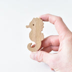 Hand holding handmade oak seahorse drawer knob showing natural wood grain and ocean animal shape