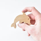 Hand holding handmade oak dolphin drawer knob showing natural wood grain and ocean animal shape