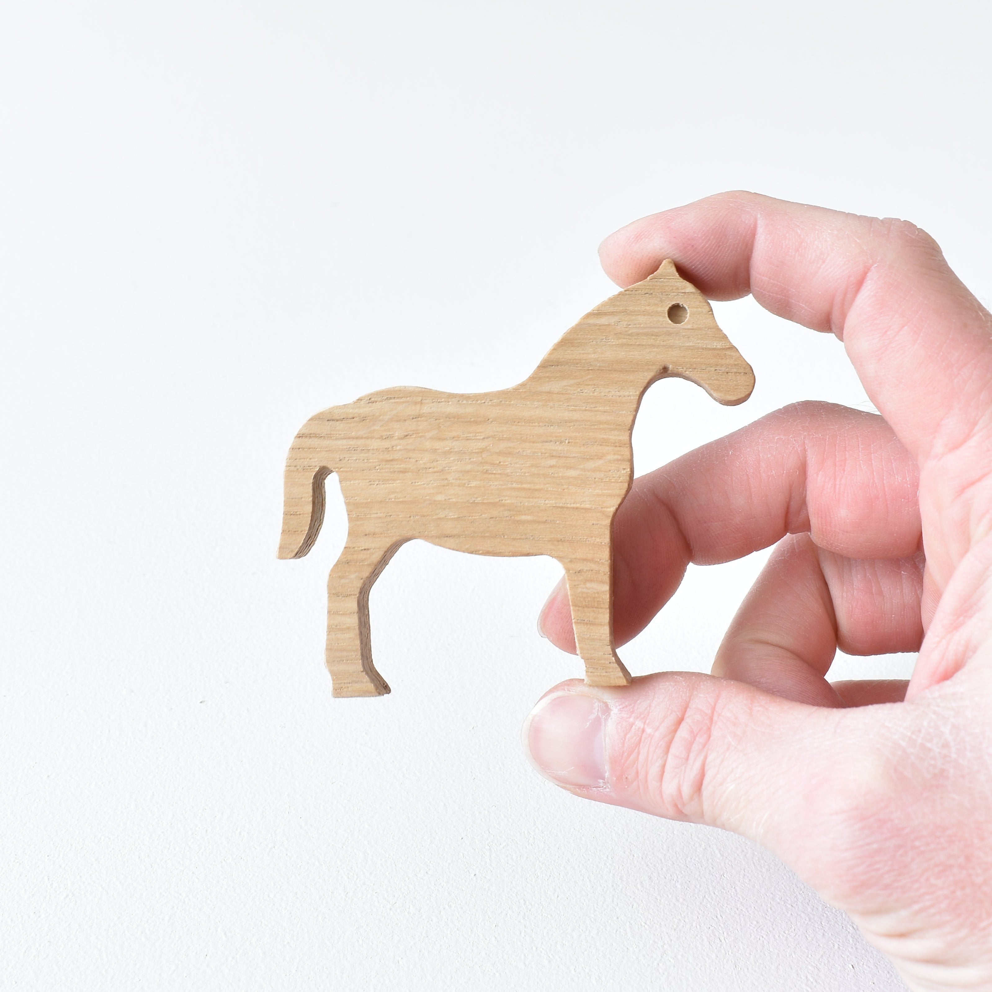 Hand holding handmade oak horse drawer knob showing natural wood grain and shape