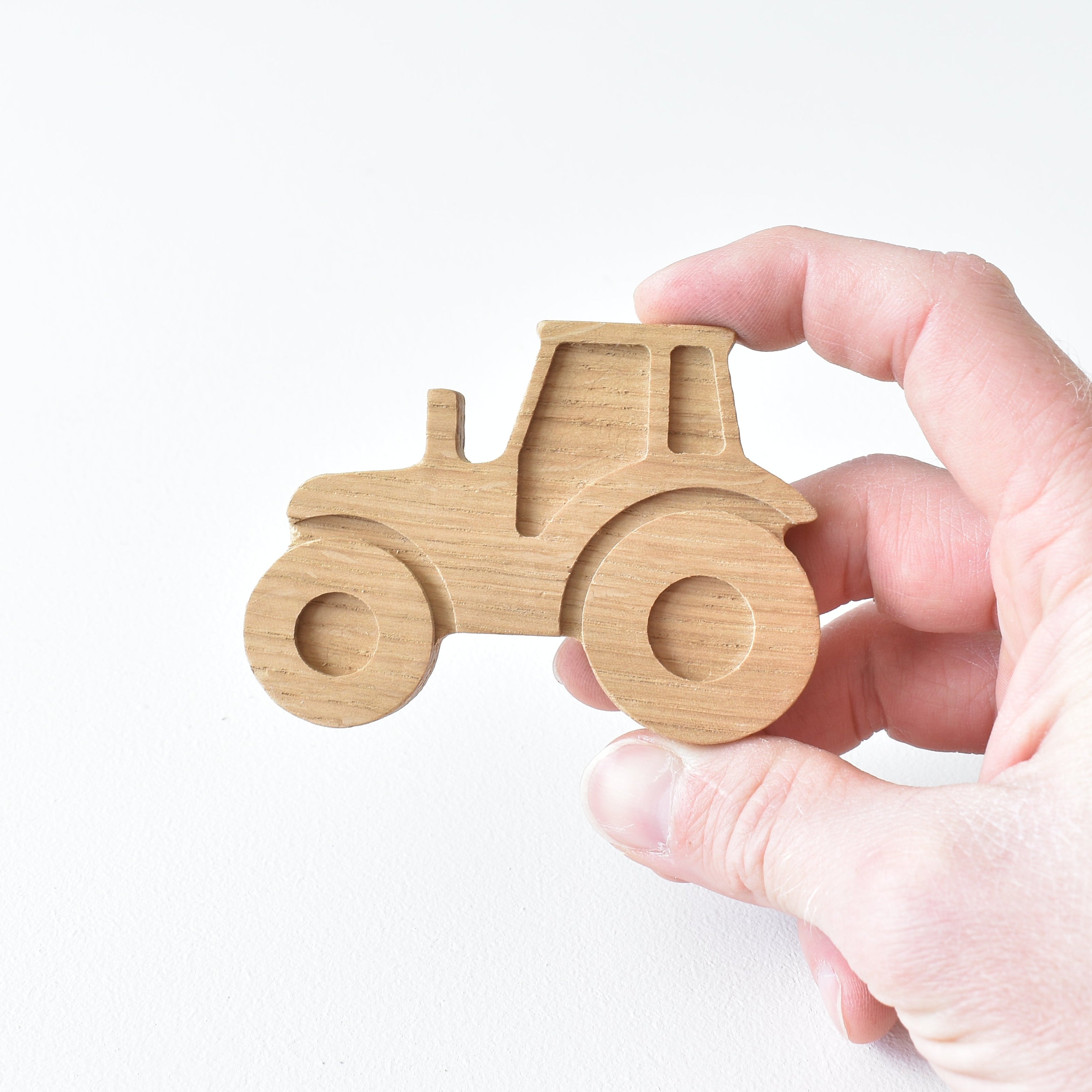 Hand holding handmade oak tractor drawer knob showing the wood grain and engraved detail