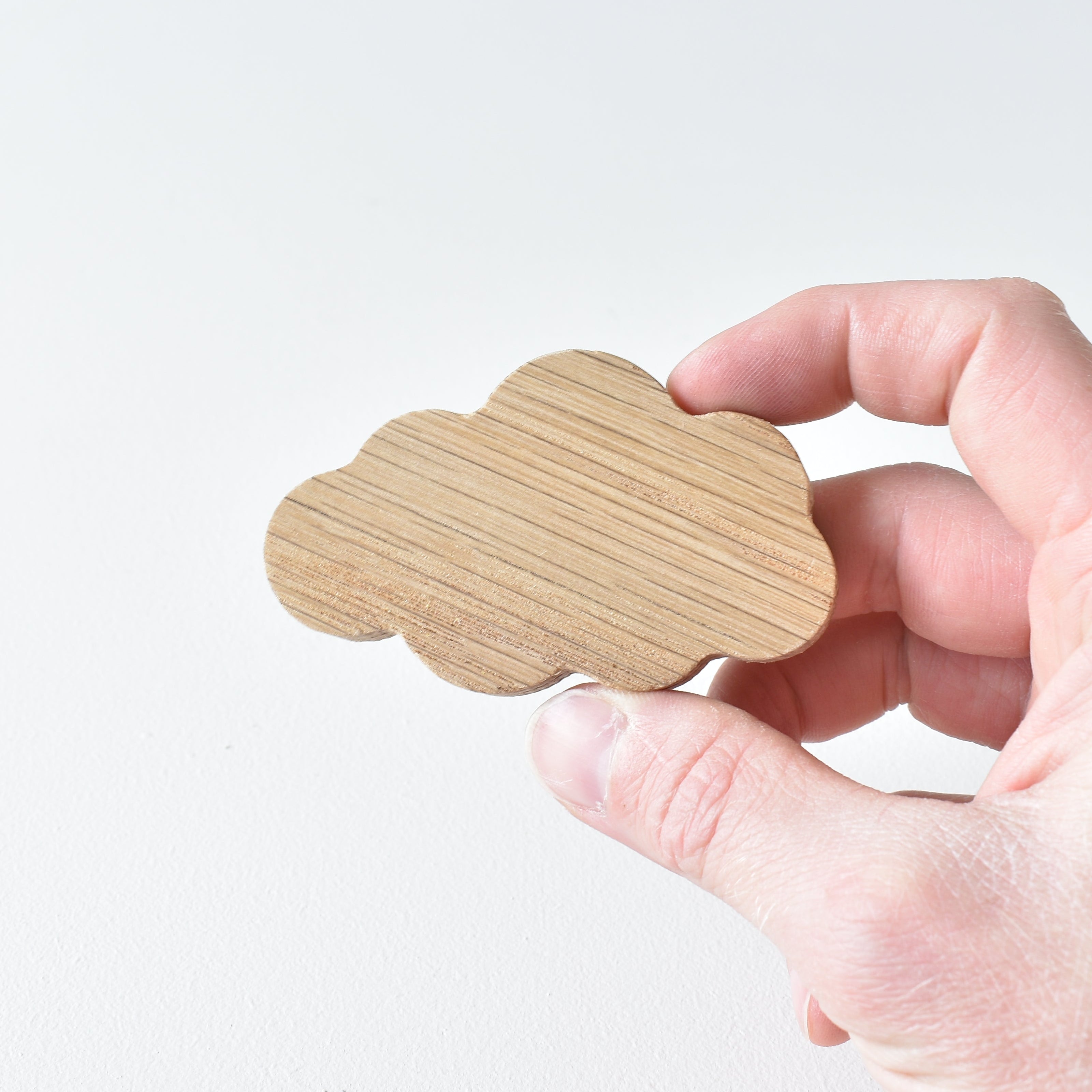 Hand holding handmade oak cloud drawer knob showing natural wood grain and soft rounded shape
