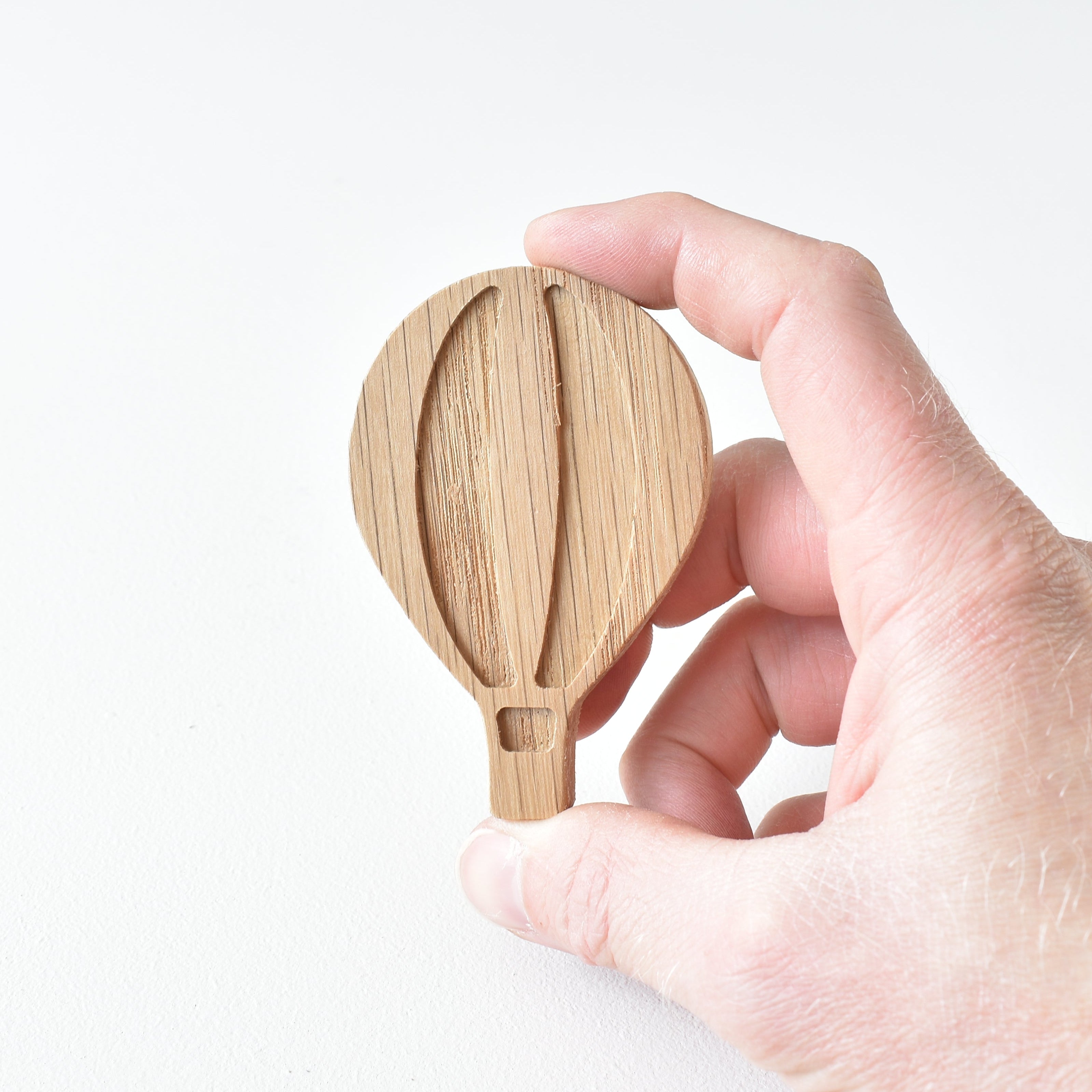 Hand holding oak hot air balloon drawer knob showing engraved detail and natural wood grain
