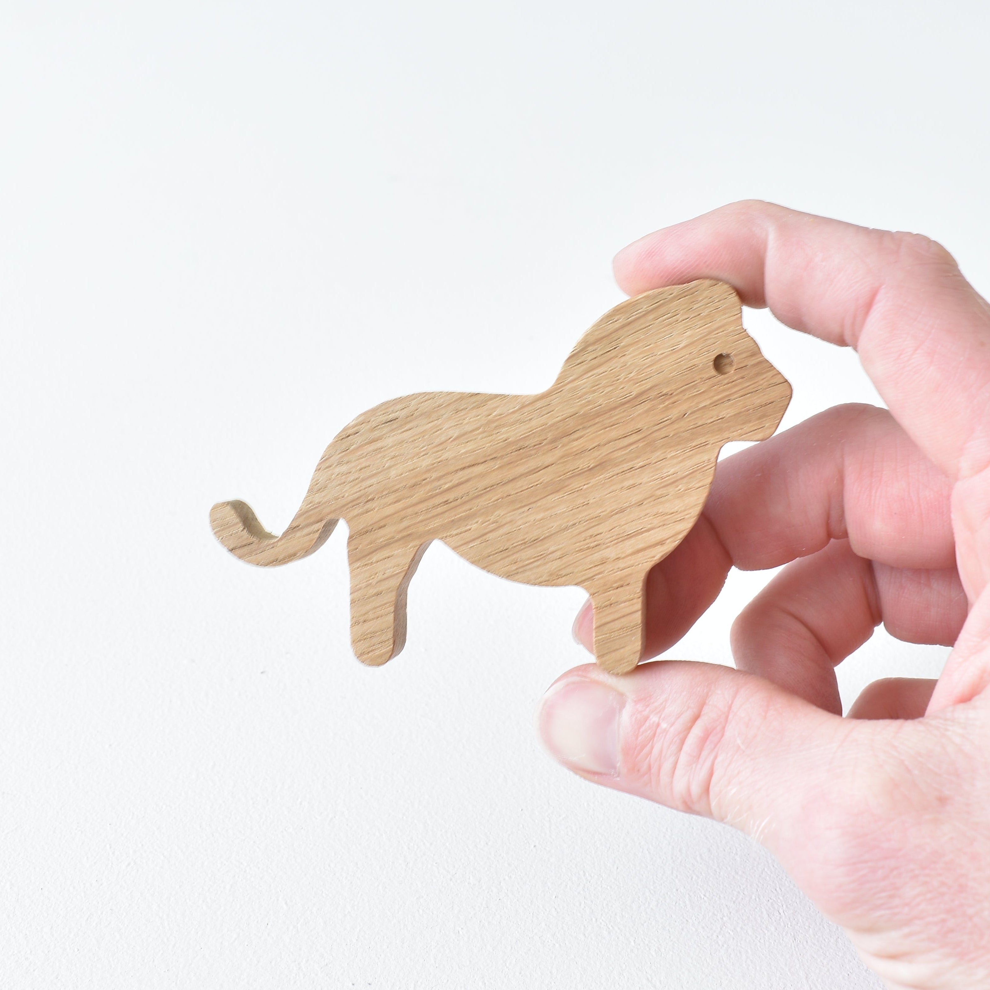 Hand holding handmade oak lion drawer knob showing natural wood grain and safari animal shape
