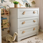Oak dinosaur drawer knobs fitted to a white nursery chest of drawers in a children’s bedroom